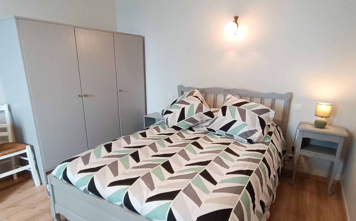 A bedroom with a bed, a wardrobe, a bedside table with a lamp, and a wall-mounted light fixture.