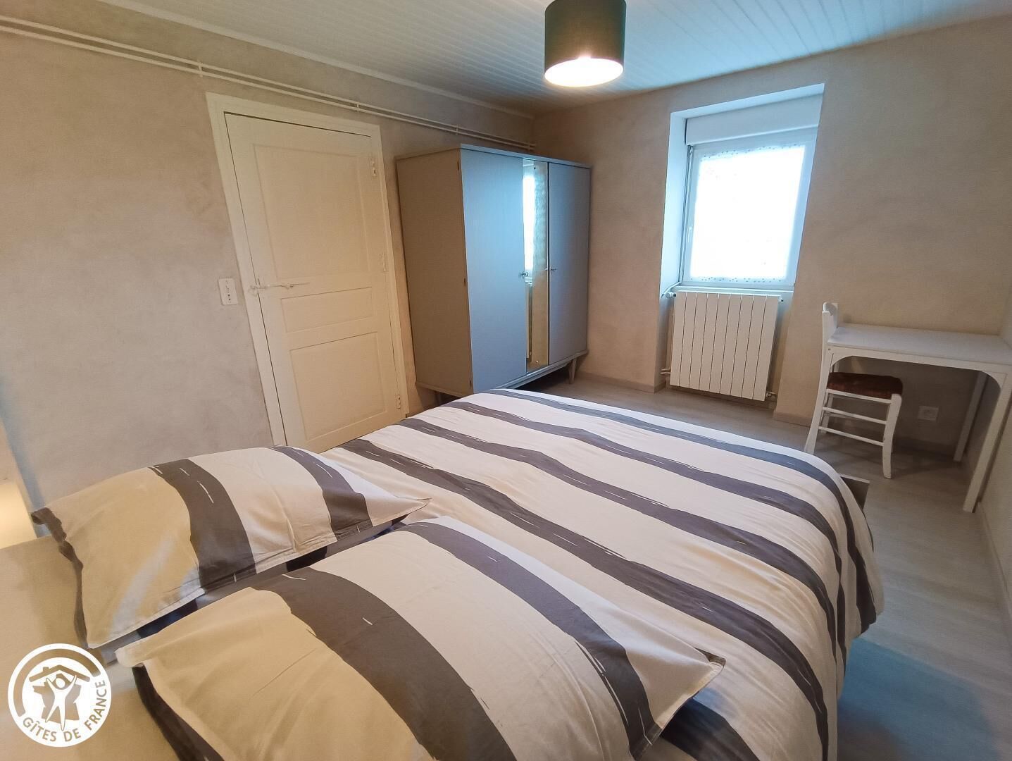 A bedroom with a bed, a wardrobe, a desk, and a window.