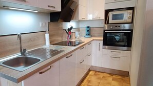 A modern kitchen with a stainless steel sink, white cabinets, a microwave, and an oven. - Gîtes de France® - Gîte de Lacroux (LINAC)