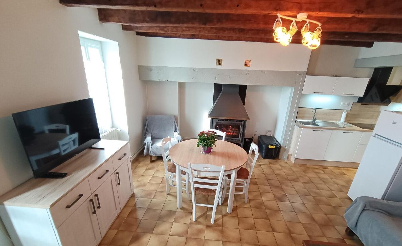 A compact kitchen with a dining table, a TV on a cabinet, and a chimney.