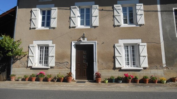 A two-story building with a brown facade, white window shutters, and a central entrance door. - Gîtes de France® - Gîte de Lacroux (LINAC)