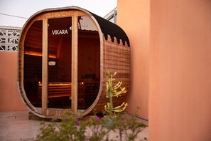 A wooden barrel-shaped structure with the name 'VIKARA' on the door, a small cactus plant outside, and a tiled floor.