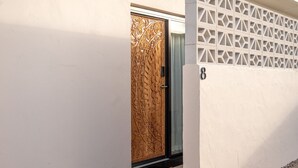 Entrada de un edificio moderno con una puerta de madera decorativa, una pared de concreto con patrones geométricos y una pequeña alfombra en la base.