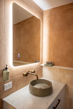 A bathroom with a round sink, a mirror, and a towel rack.