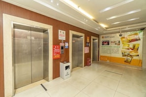 Zona de ascensores con dos elevadores, un cubo de basura y una pared con carteles informativos.