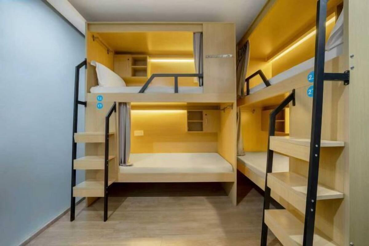 Dormitorio con literas, suelo de madera, barandillas de metal y una pequeña estantería.