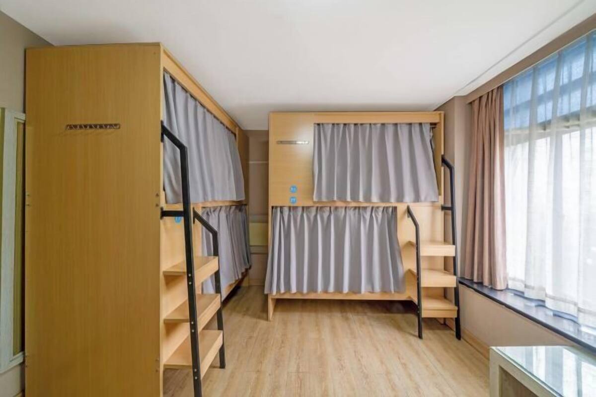 Una habitación con literas, una puerta de madera, una mesita y una ventana con cortinas.