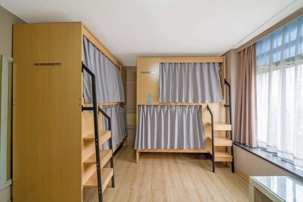 Ein Zimmer mit Etagenbetten, einer Holztür, einem kleinen Tisch und einem Fenster mit Vorhängen.