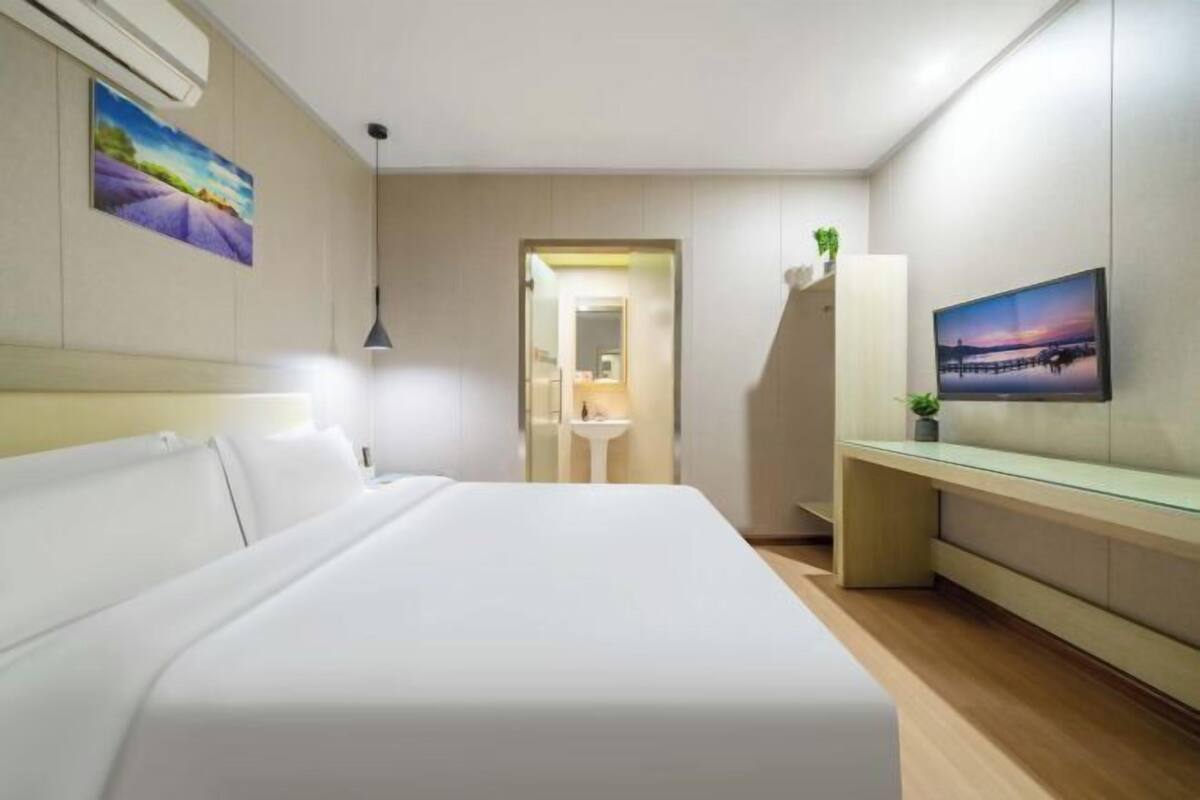 Habitación de hotel con cama, mesita de noche, televisión y baño visible a través de una puerta abierta.