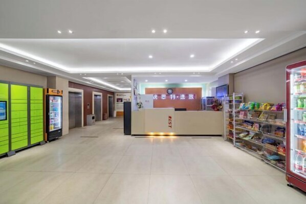 Zona de recepción de hotel con un mostrador, una máquina expendedora y un quiosco de autoservicio.