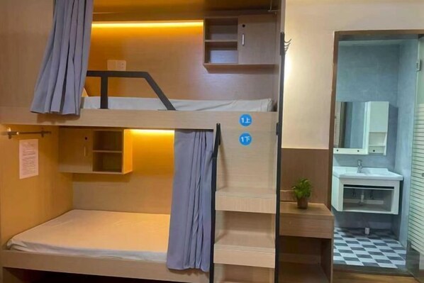 Habitación con literas, un armario pequeño y un lavabo en el baño contiguo.