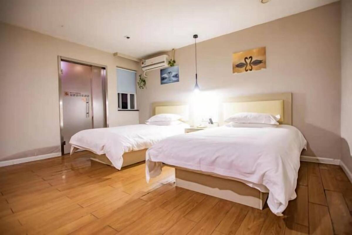 Habitación de hotel con dos camas, piso de madera, ventilador de techo y una puerta con un letrero.