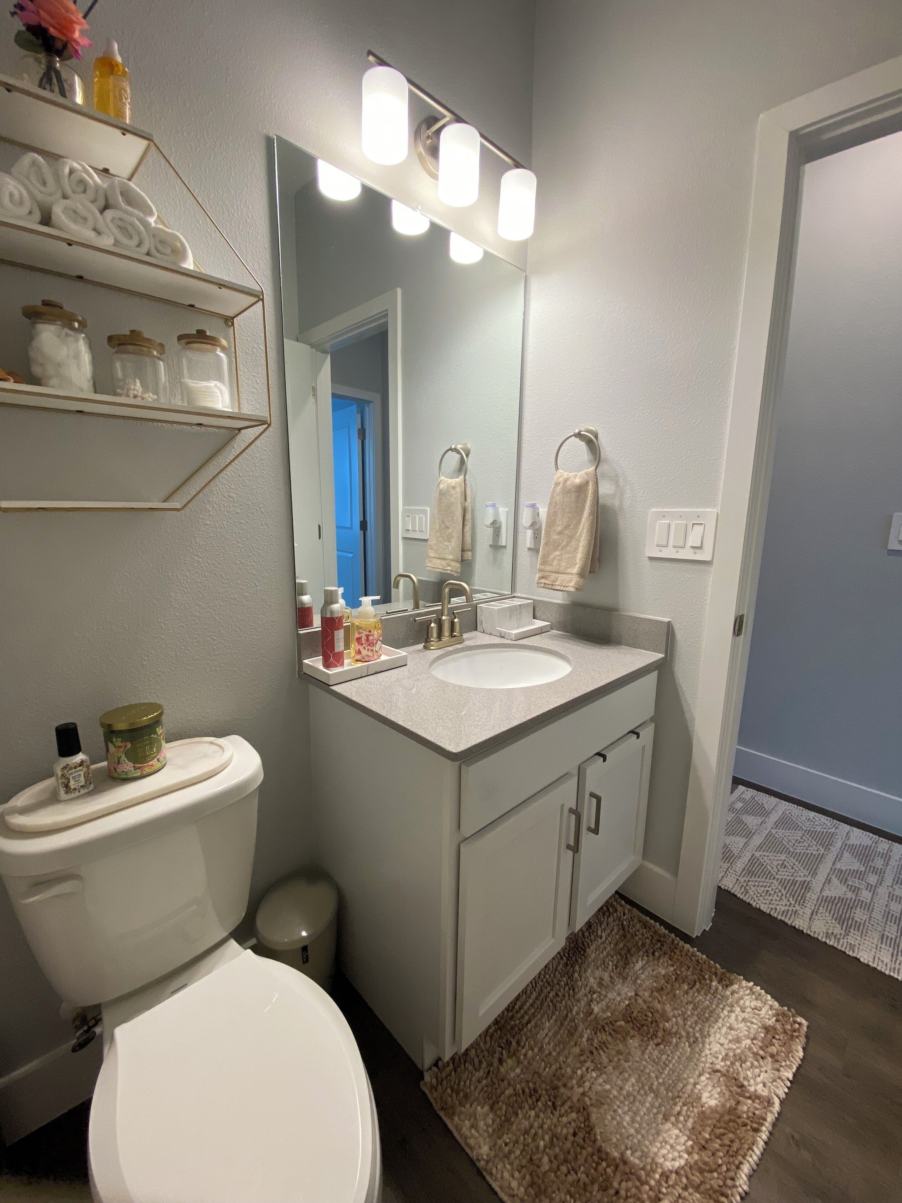A bathroom with a toilet, sink, and mirror. There are shelves with towels and toiletries.