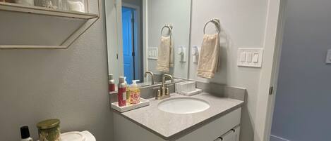 A bathroom with a toilet, sink, and mirror. There are shelves with towels and toiletries.