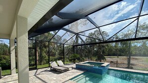 A covered outdoor area with a swimming pool, lounge chairs, and a hot tub.