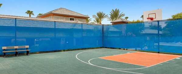 Ein Basketballplatz im Freien mit blauem Zaun, einer hölzernen Bank und einem Basketballkorb.