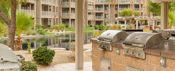 Un espace cuisine extérieur doté de plusieurs barbecues, d’un petit étang et offrant une vue sur un immeuble à plusieurs étages avec des balcons.