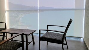 Un balcon avec vue sur une plage et des montagnes, comprenant une table et deux chaises.