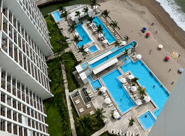 A resort with multiple swimming pools, a beach, and a high-rise building.