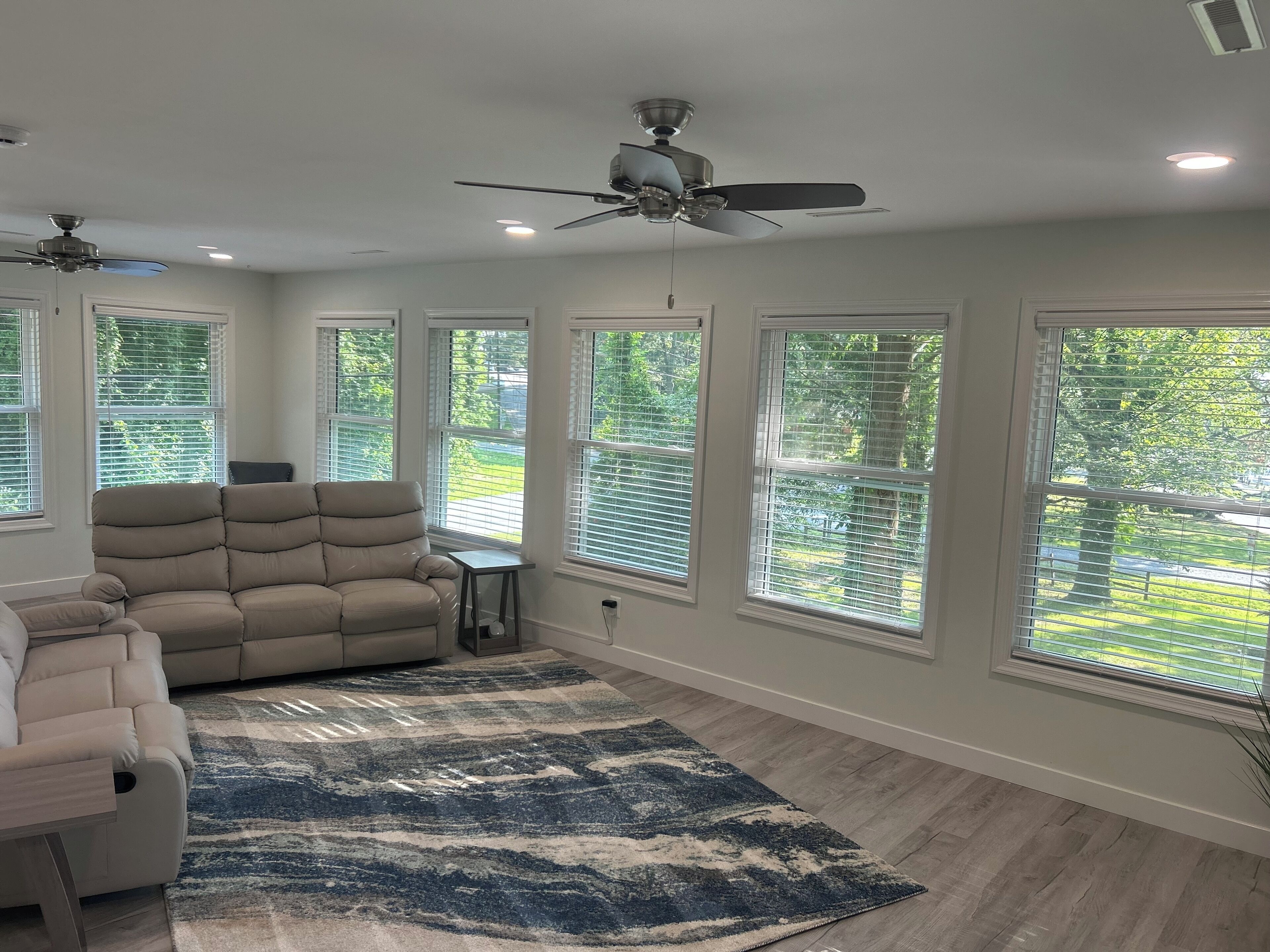 A spacious living room with a large beige sectional sofa, a blue patterned rug, and a ceiling fan.