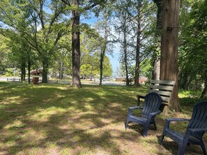 Un parque con un banco y sillas Adirondack, rodeado de árboles y un cielo despejado.