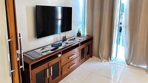 A modern living room with a flat-screen TV, wooden cabinet, and an air conditioning unit.