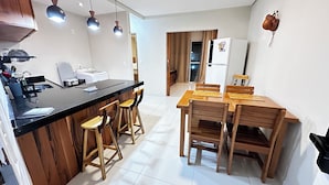 A compact kitchen with a black countertop, wooden stools, and a wooden dining table with chairs.