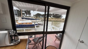 A small room with a sliding glass door leading to a deck with outdoor seating and a view of boats on a body of water.
