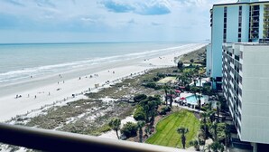 Blick auf einen Strand mit Hotelgebäude, Sand und Meer.