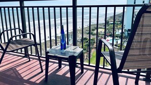 Ein Balkon mit Blick auf Strand und Meer. Zwei Stühle und ein kleiner Tisch mit einer Flasche und einem Glas.