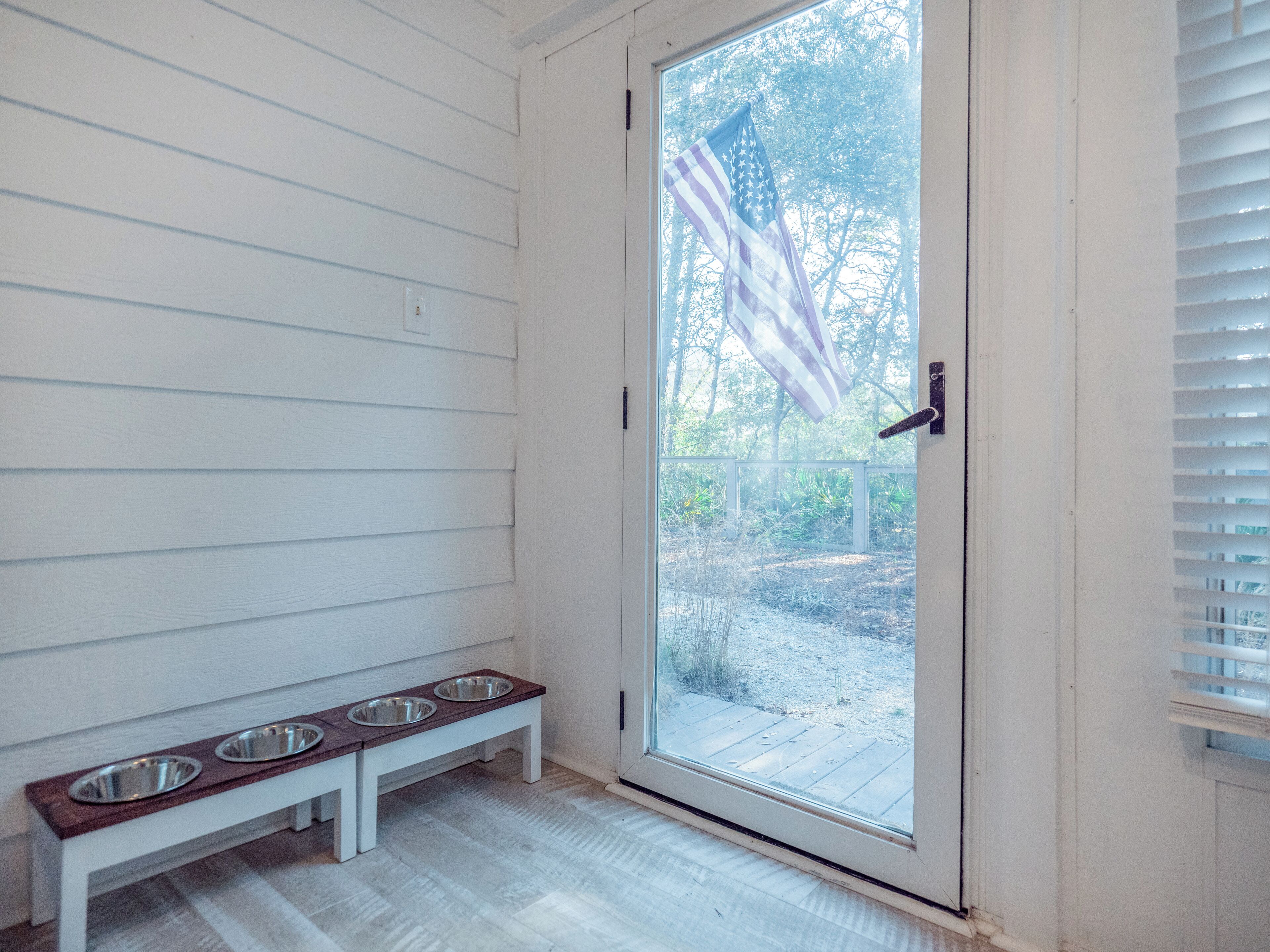 A room with a white door, a bench with two metal bowls, and an American flag hanging by the door.