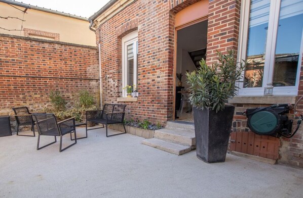 Un bâtiment en briques doté d’un patio comprenant un espace extérieur avec des sièges et un grand bac à fleurs.