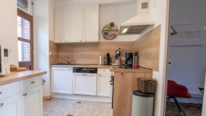 Una cocina compacta con armarios blancos, una encimera de madera, una cafetera y un cubo de basura.