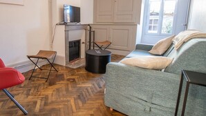 Una sala de estar con chimenea, un sofá gris, un sillón rojo y un televisor sobre un mueble.