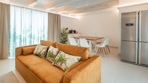 Ein modernes Wohnzimmer mit einer Couch, einem Esstisch, Stühlen und einer Küchenzeile mit einem Kühlschrank.