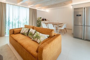 Un salon moderne comprenant un canapé, une table à manger, des chaises et un coin cuisine avec un réfrigérateur.