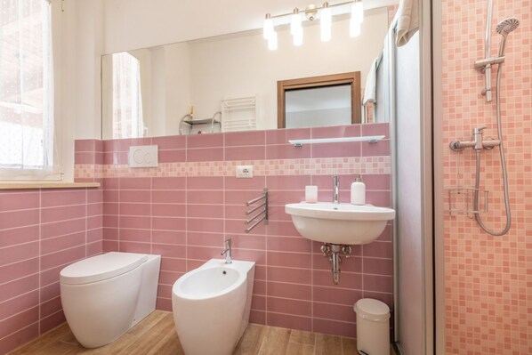 A bathroom with a bidet, toilet, sink, and shower.