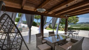 Eine Terrasse im Freien mit Korbmöbeln, einem Tisch mit Glasplatte und Blick ins Grüne.