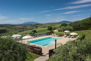 Area piscina con lettini e ombrelloni, circondata da una recinzione in legno e vegetazione rigogliosa.
