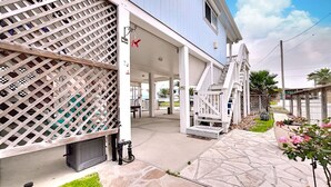 A covered outdoor area with a staircase leading to a covered porch, stone flooring, and a lattice fence.
