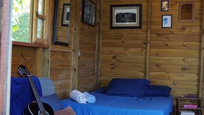 A cozy cabin room with a bed, a couch, and a guitar. - Solitude Cabin - Sailor (Pântano do Sul)