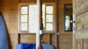A wooden cabin interior with a bed, a guitar leaning against the wall, and a window with natural light. - Solitude Cabin - Sailor (Pântano do Sul)