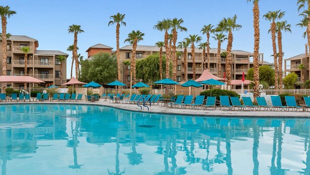 A swimming pool with lounge chairs and umbrellas, surrounded by palm trees and multi-story buildings. - 2-bedroom resort in fabulous Indio with fitness room, AC. Relax and enjoy (Indio)