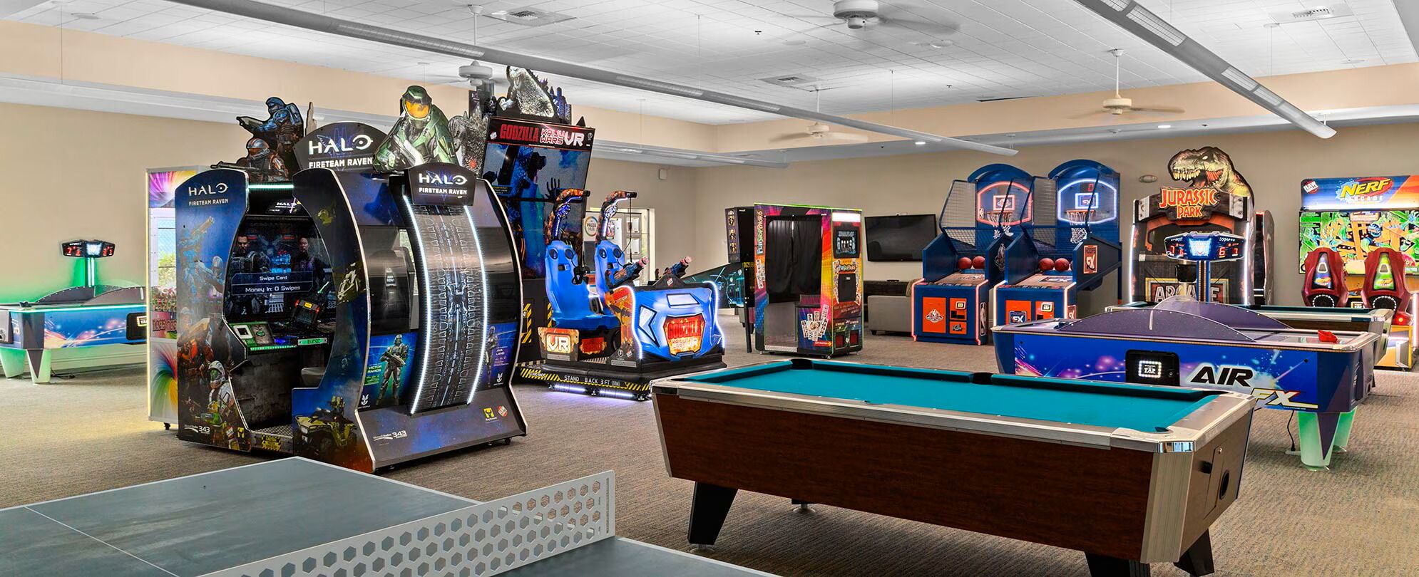Ein Indoor-Erholungsbereich mit verschiedenen Spielgeräten, darunter ein Billardtisch und Spielautomaten.