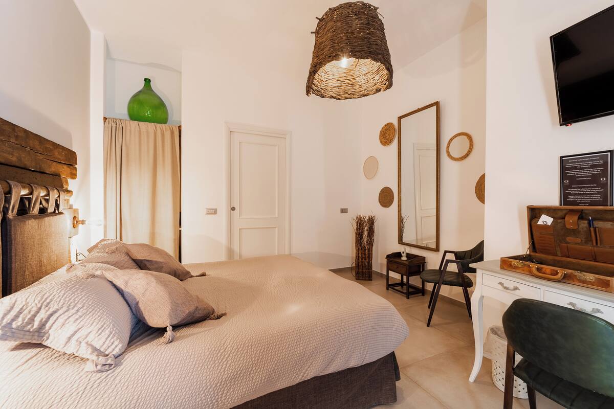 Un dormitorio con cama, escritorio, silla, espejo y televisor.