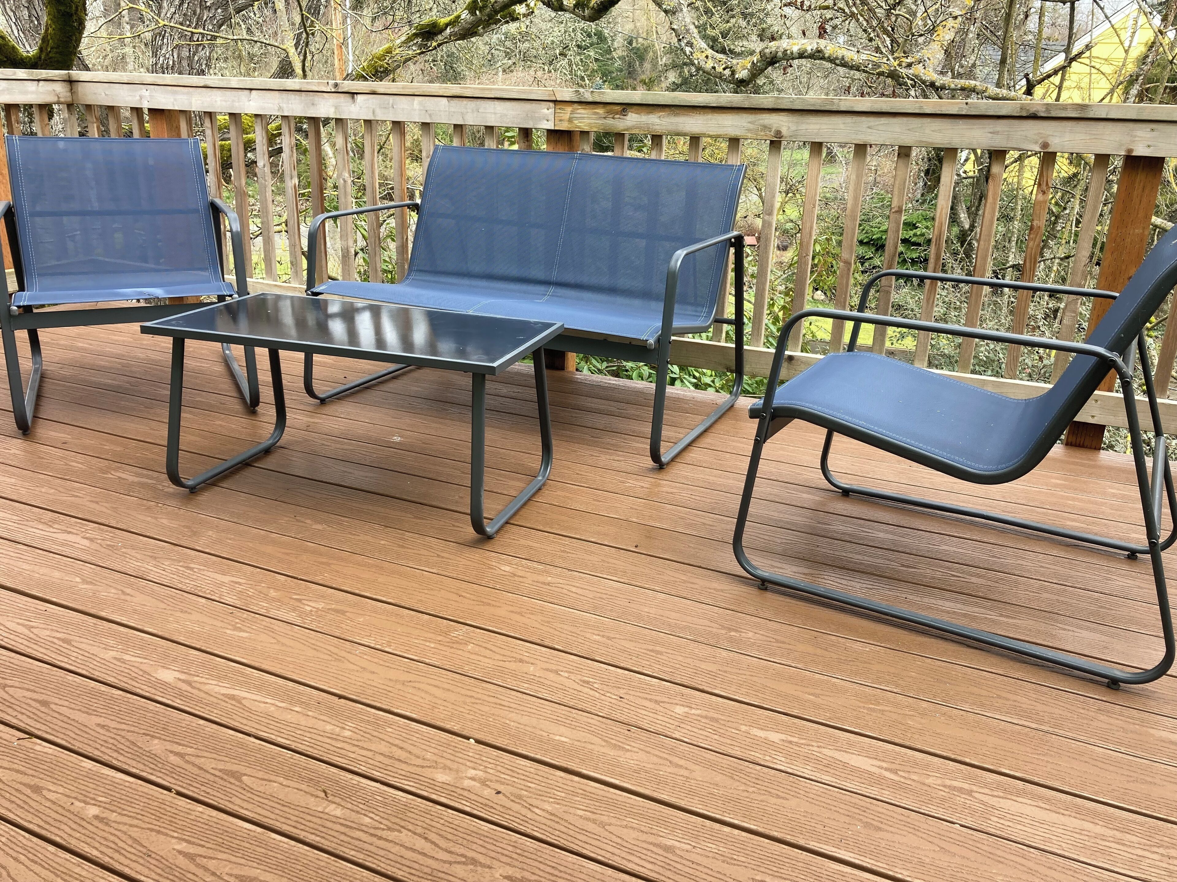 Eine Holzterrasse mit einem Metalltisch und drei blauen Stühlen.