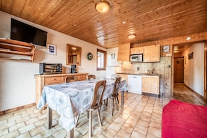 Une cuisine chaleureuse avec des meubles en bois, une table à manger avec des chaises, un téléviseur et un four à micro-ondes.