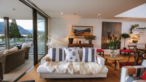 A modern living room with a sofa, chairs, a dining table, and a large window overlooking a mountainous landscape. - Nautilus - Sleeps 8 - Lake Views (Wanaka)