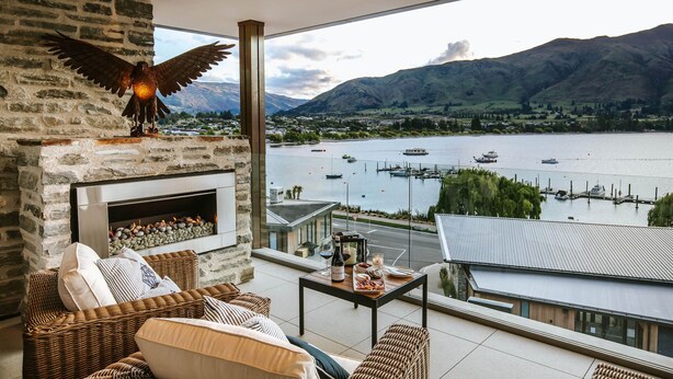 A balcony with wicker furniture, a fireplace, and a view of a lake with boats. - Nautilus - Sleeps 8 - Lake Views (Wanaka)