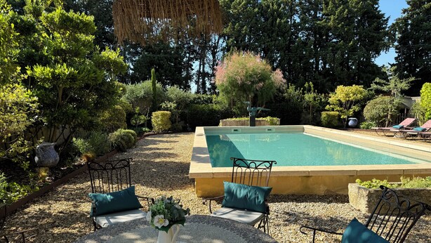 Un área de piscina con un suelo de baldosas, sillas de descanso y un jarrón decorativo.